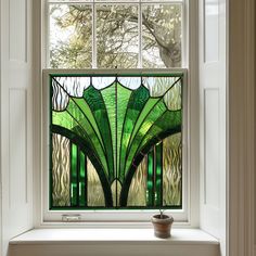 a green stained glass window sitting on top of a white shelf next to a potted plant