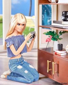 a barbie doll sitting on the floor with a camera in her hand and looking at it