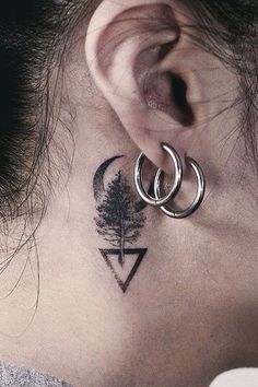 a woman's neck has a small tree and two rings on her left ear