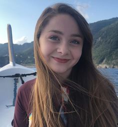 a girl with long brown hair wearing a neck tie and smiling at the camera on a boat