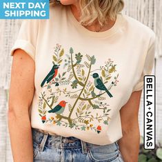 Introducing our Cottagecore Birds and Flowers Shirt, a perfect blend of nature and vintage. This Folk Art Scandi Art T Shirt features beautiful bird and flower designs that capture the essence of serene, countryside living. Available in Plus Sizes and Oversized T-Shirts, this vintage tee ensures a comfortable and stylish fit for everyone. Whether you're looking for a unique Bird Gift or a special Gift For Her, this shirt is sure to delight. Embrace the Cottage core aesthetic with this timeless piece that combines elegance with a touch of nature-inspired artistry. -Size Chart - Please refer to the last image 🪨Medium weight material -Unisex relaxed fit -Free shipping on orders over $35 in the USA -100% Ring-spun cotton -Machine wash inside out in cold water. Tumble dry low -Do not iron -Mad Nature-inspired Cotton Tops With Screen Print, Nature-inspired Crew Neck Tops With Screen Print, Nature-inspired Cotton Tops With Graphic Print, Nature-inspired Graphic Print Crew Neck Top, Nature-inspired Cotton T-shirt With Screen Print, Scandi Art, Countryside Living, Special Gifts For Her, Gifts Vintage