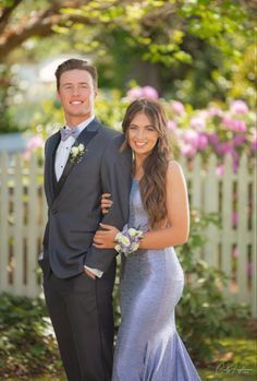 a man and woman in formal wear standing next to each other near a white picket fence