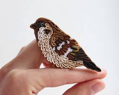 a bird brooch sitting on top of someone's hand in front of a white background