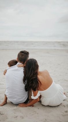 a man and woman sitting on the beach with their back to each other, looking out at the ocean