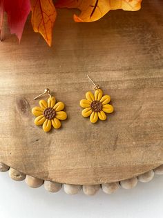 two yellow flower earrings sitting on top of a wooden table next to an autumn leaf