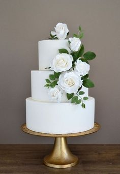 a three tiered cake with white flowers on top and green leaves on the bottom