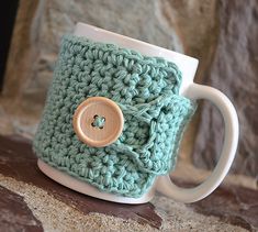 a crocheted coffee cup holder with a button on it