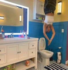 a woman standing on top of a white toilet in a bathroom next to a sink