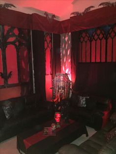 a living room filled with black furniture and red curtains on the windows above it is a coffee table that has candles in front of it