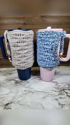 two crocheted coffee mugs sitting next to each other on a marble counter