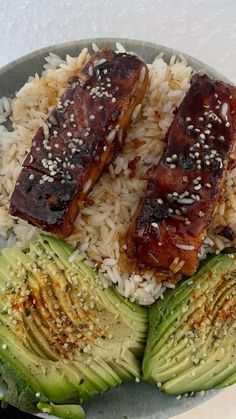 two pieces of meat on top of rice and cucumber slices with sesame seeds