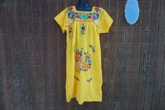 "A fun summery Mexican fiesta dress in yellow with colorful floral embroidery. Styling perfect for warm sunny days.  Labeled size \"G\" Grande - please refer to measurements below for sizing. Condition has a few spots in the back shown in last photo.  MEASUREMENTS (taken with the garment laid flat) Underarm to underarm- 23 inches Waist- 27 inches across front Length: 45 inches I believe this would fit a modern day large comfortably." Traditional Yellow Embroidered Dress For Spring, Yellow Embroidered Dress For Vacation, Traditional Yellow Embroidered Dress For Summer, Yellow Embroidered Dress With Short Sleeves For Summer, Summer Fiesta Yellow Dress, Bohemian Yellow Embroidered Dress With Short Sleeves, Traditional Yellow Floral Embroidered Dress, Traditional Yellow Embroidered Summer Dress, Spring Yellow Embroidered Dress With Short Sleeves