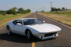 a white car is parked on the side of the road in front of a grassy field