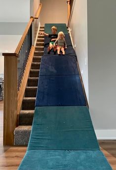 two children are sitting on the blue mat under the stairs