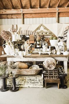 an old table with many items on it in a room filled with plants and other things