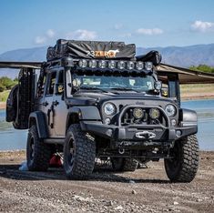 the jeep is parked by the water with its lights on