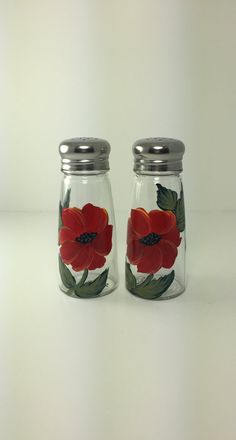 two glass jars with red flowers painted on the lids and one has a silver lid