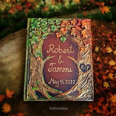 a wedding album is sitting on a tree stump with autumn leaves around it and the words robert & tammi written in cursive