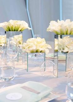 there are many vases with flowers in them on the dining room table set for an event