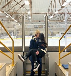 a man and woman kissing on the side of a bench in front of an ice rink