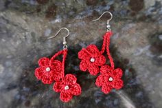 red crocheted flower earrings with pearls on them sitting on top of a rock