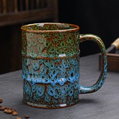 a blue and green coffee mug sitting on top of a table next to some nuts