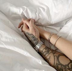 a person laying in bed with their arm wrapped around each other and tattoos on their arms