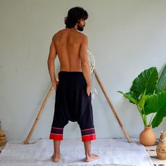 a man with no shirt standing in front of a white wall next to a potted plant