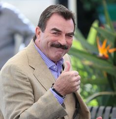 a man with a mustache giving the thumbs up