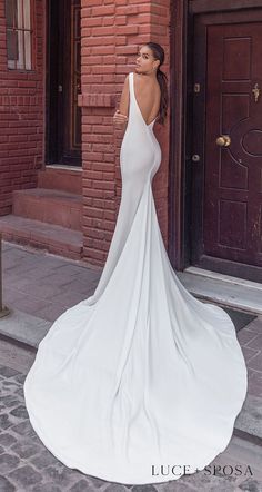 a woman standing in front of a brick building wearing a white dress with open back