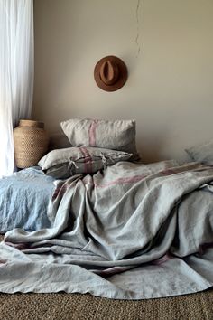 an unmade bed with a hat on the wall