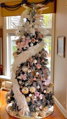 a decorated christmas tree with white feathers and pink flowers in the center is sitting on a wooden floor