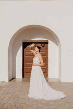 a woman standing in front of a doorway wearing a white dress and holding a hat