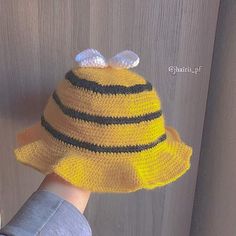 a child's hand wearing a knitted yellow hat with black stripes and a bee on top