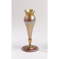 a gold colored vase sitting on top of a white table next to a candle holder