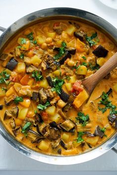 a pot filled with stew and vegetables on top of a table next to a wooden spoon