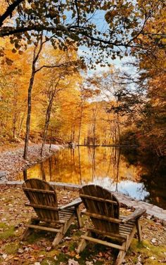 two wooden chairs sitting on top of a grass covered field next to a body of water