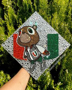 a hand holding a graduation cap with a bear on it