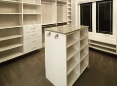 an empty walk - in closet with white shelving and marble counter top, next to a window