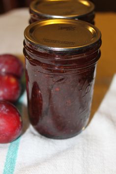 three jars filled with plum jam sitting on top of a white table cloth next to two red apples