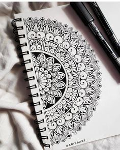 a notebook with an intricate design and two black markers on the page next to it