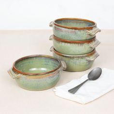 four green bowls with spoons sitting next to each other on top of a table