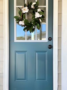 a blue front door with a wreath on the top and two white flowers hanging from it