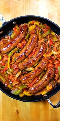 sausages and peppers in a skillet on a wooden table with tongs next to it