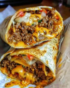 two burritos sitting on top of each other covered in cheese and ground beef