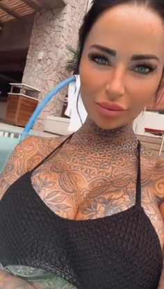 a woman with tattoos on her arm and chest standing in front of a swimming pool