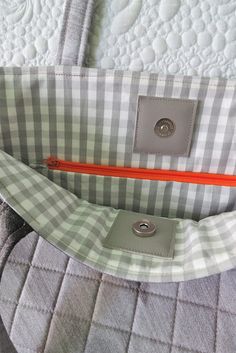 a close up of a purse on a bed with the zipper open and an orange handle