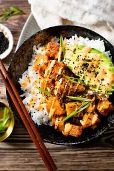 a black bowl filled with rice and chicken next to chopsticks