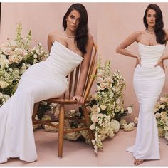 two beautiful women in white dresses sitting on chairs next to flowers and greenery, posing for the camera