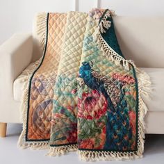 a white couch sitting next to a colorful blanket on top of a wooden table in front of a white wall